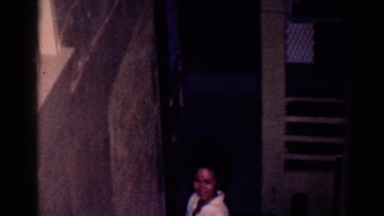 Dim interior with a woman partly visible near a doorway and dark wall openings.