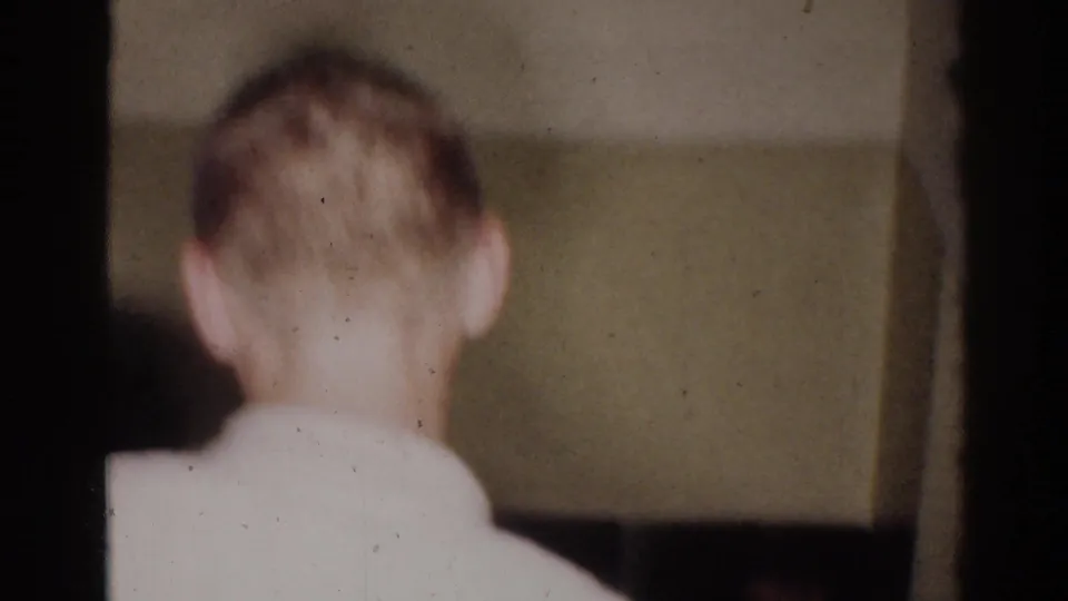 1966 El Monte home-movie frame showing a blond young martial arts student from behind in a white uniform indoors.