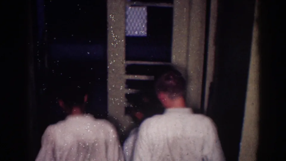 Judo athletes in white gis are partially visible from behind near a doorway and patterned window glass in the dim interior.