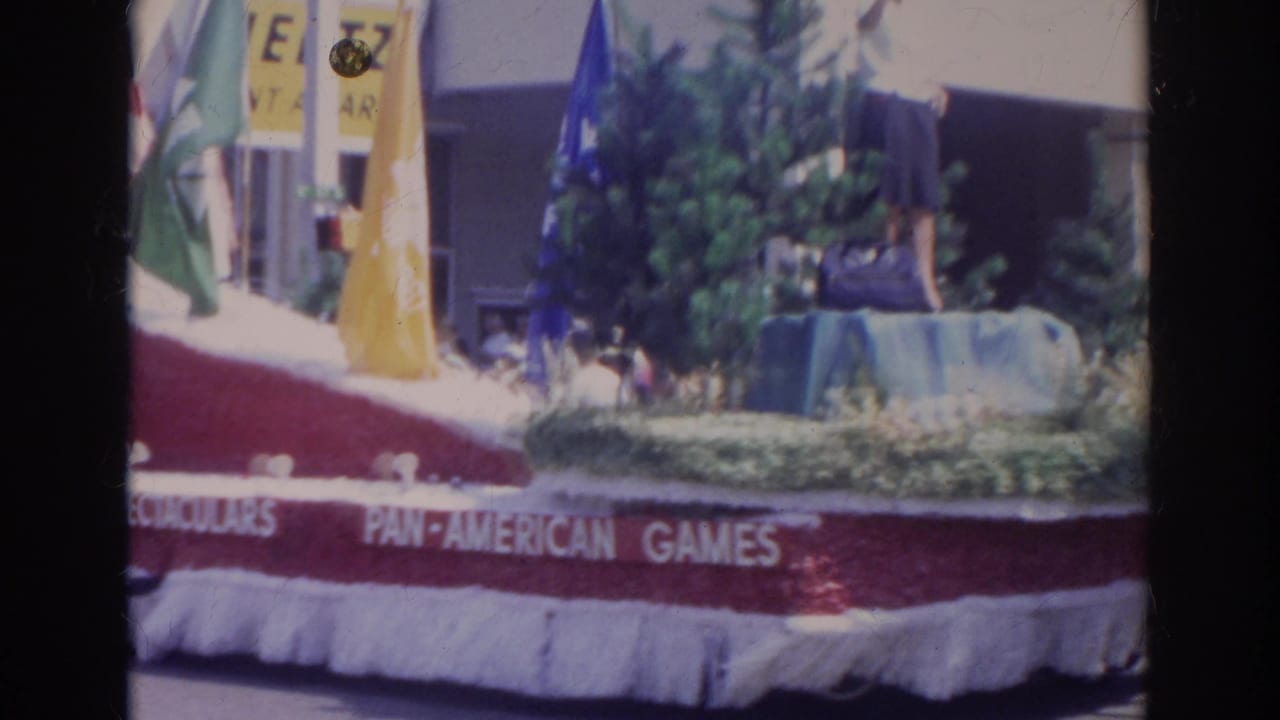 1966 Norfolk parade view of a float side reading Pan-American Games with trees, flags, and a person standing above spectators.
