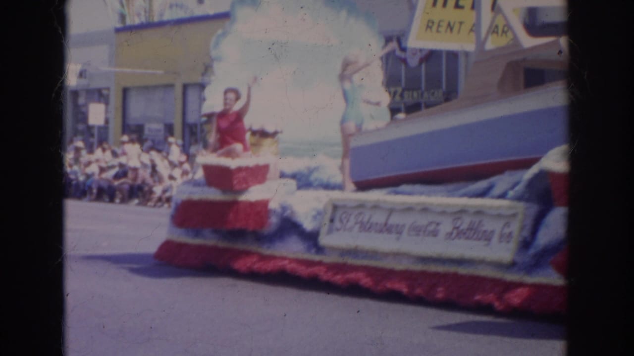 A woman waves from a patriotic float during a 1966 Norfolk parade, with curbside spectators and a Hertz sign behind her.
