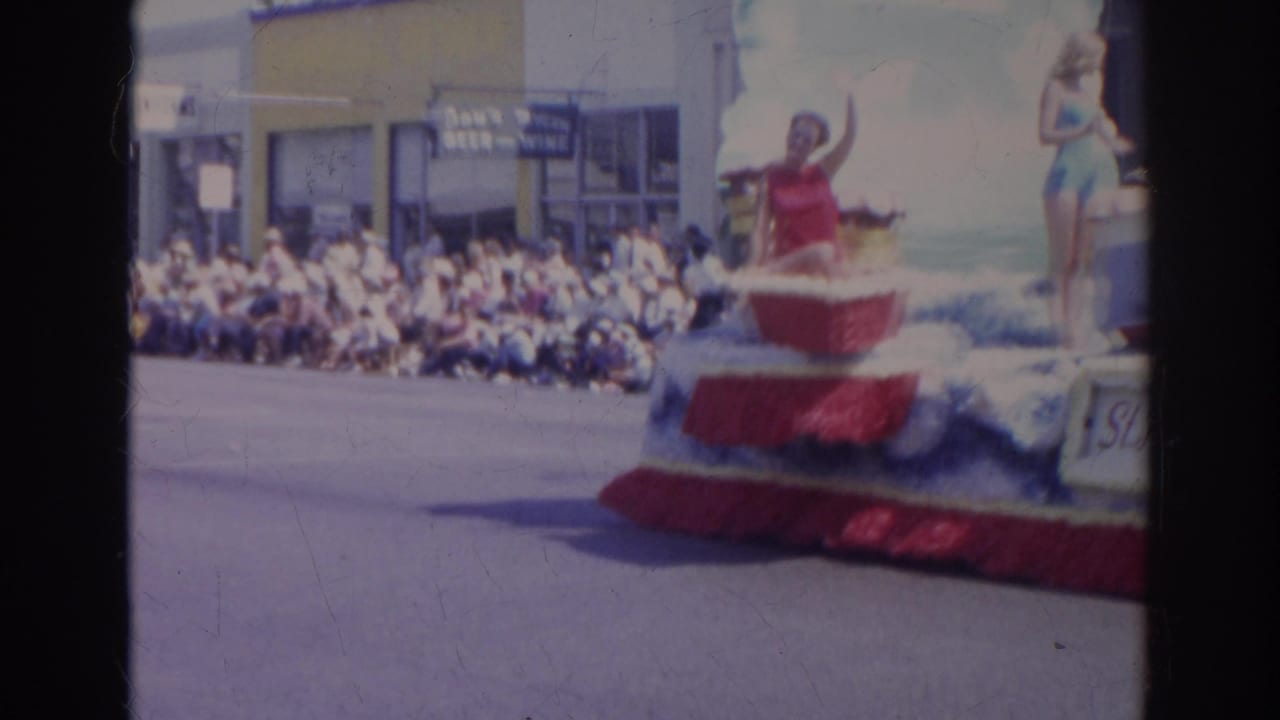 Curbside spectators watch a red, white, and blue float pass during the 1966 Norfolk parade.