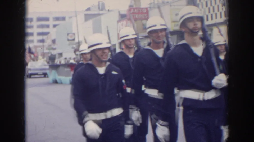 Sailors in dark blue uniforms and white helmets pass near the camera during a Norfolk, Virginia street parade in 1966.