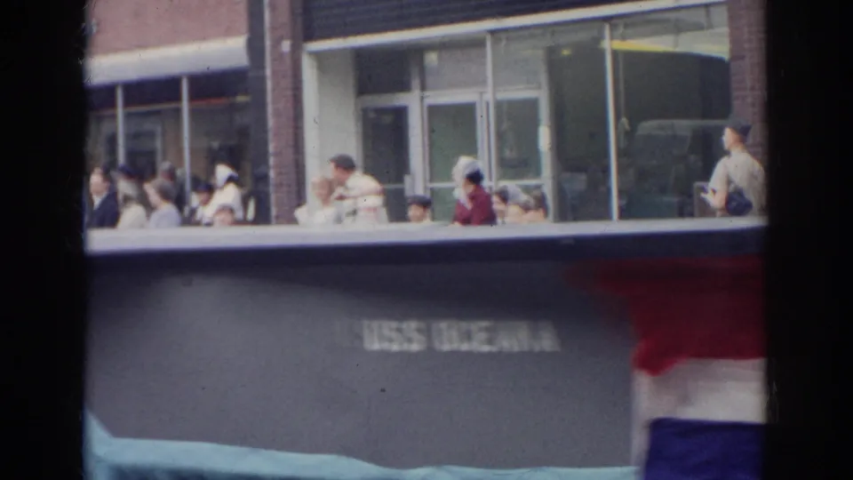 A USS Oceana parade display moves past spectators seated by a glass-fronted building in the Norfolk 1966 home-movie footage.