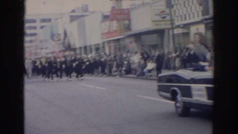1966 Norfolk street parade view with a classic convertible ahead of a uniformed marching band and spectators along storefronts.