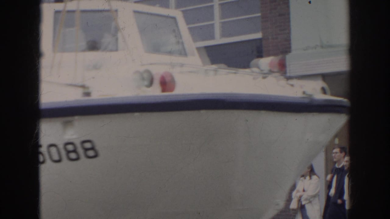 Close view of a white amphibious vehicle beside a building with people nearby.