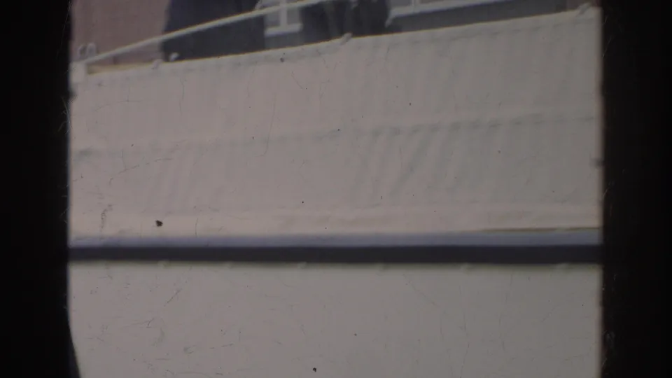 Side view of the docked amphibious vehicle, showing white hull panels, blue trim, and a canvas-covered upper area.