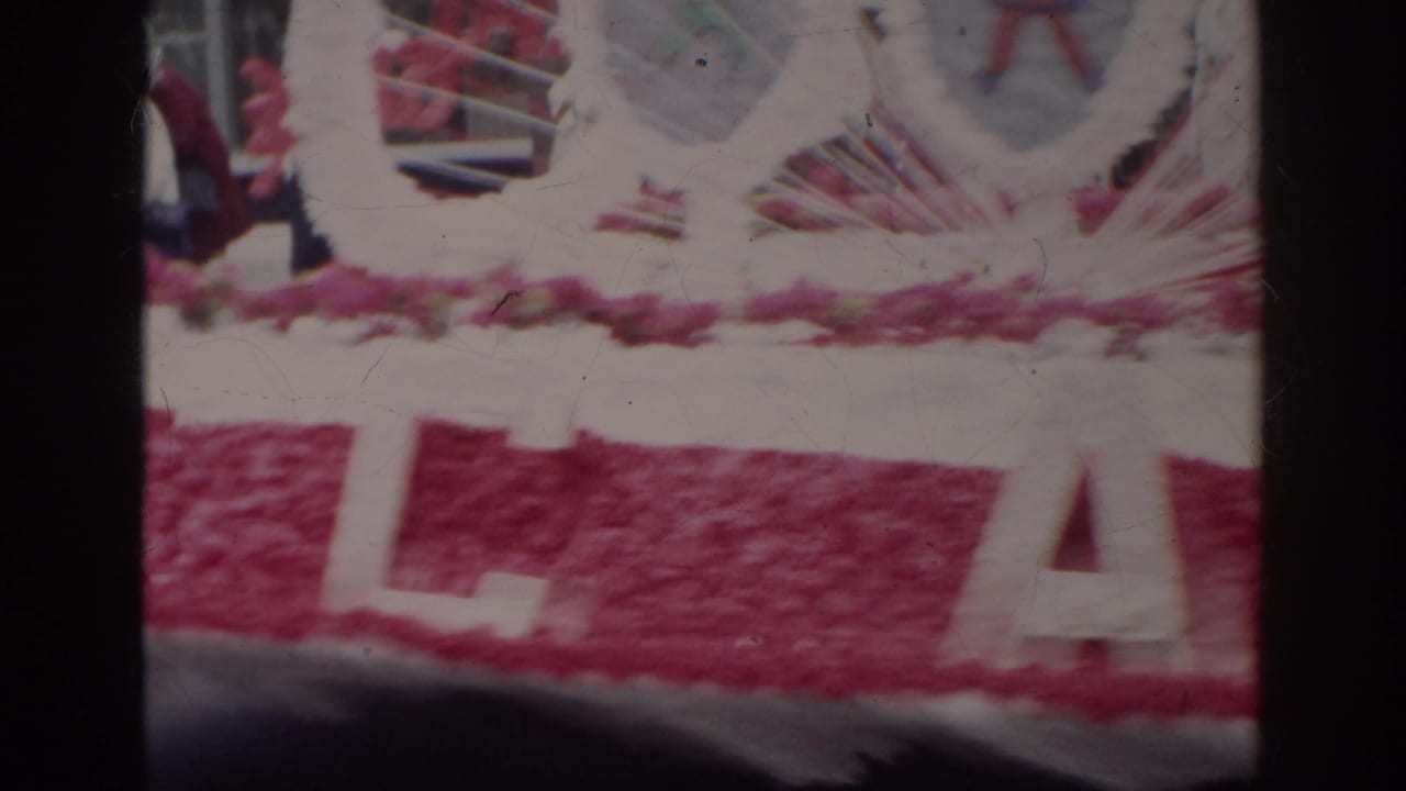 A close, soft 8mm view of the Norfolk parade float shows pink decoration and large white lettering partly obscured by the frame edge.