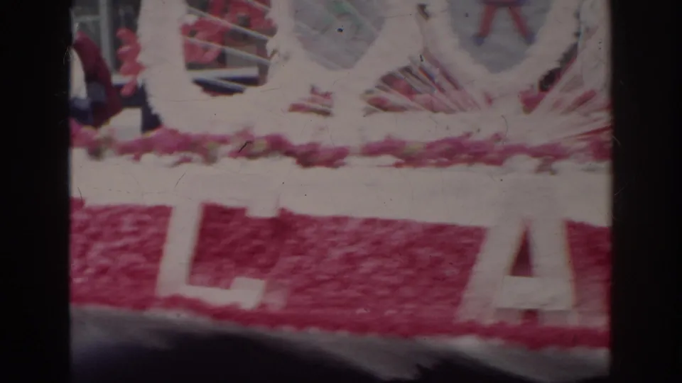A close, soft 8mm view of the Norfolk parade float shows pink decoration and large white lettering partly obscured by the frame edge.