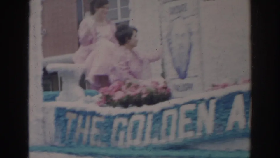 Young women ride on a decorated Norfolk parade float in 1966, with flowers, portrait panels, and a partial “THE GOLDEN A” banner visible.