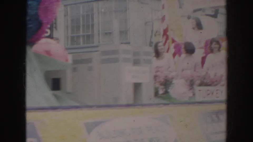 A Norfolk parade float section shows flags, floral decorations, and people standing beside the display on the street.