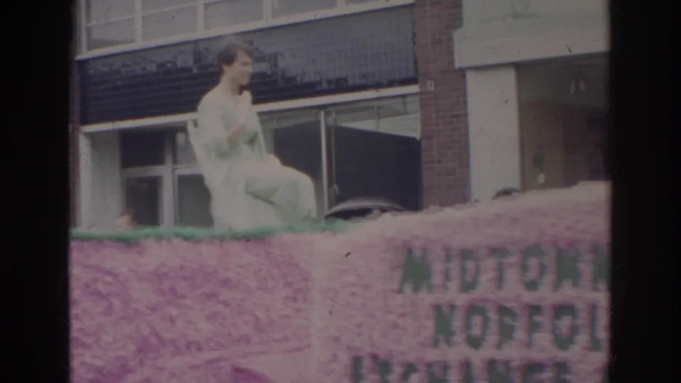 Shelley Fabares appears seated on a pink azalea parade float in Norfolk, Virginia, with brick storefronts behind her.