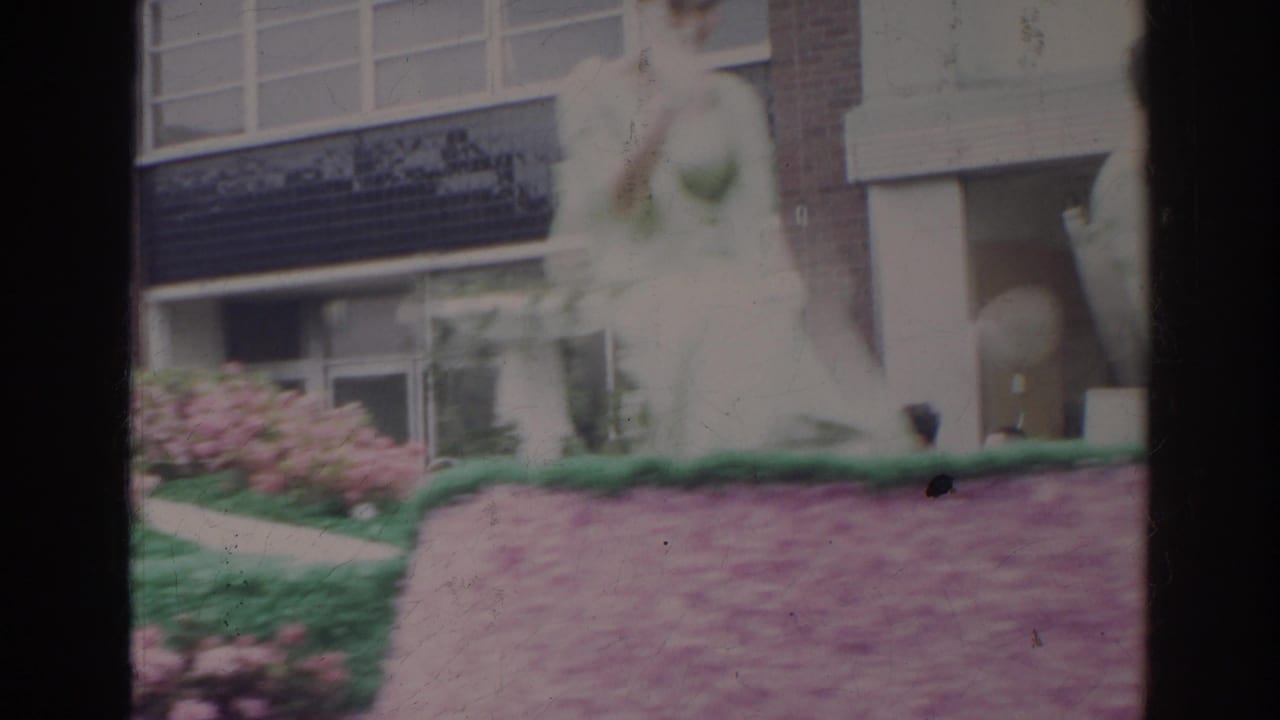 Light-dressed woman on a flower-covered float beside pink blossoms.