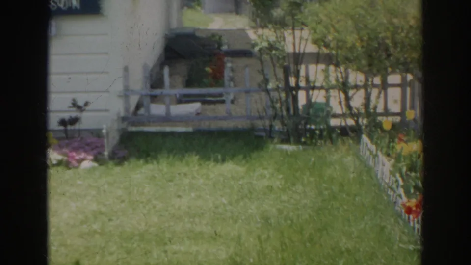 The final frame looks across the side yard toward flowers, shrubs, small steps, white siding, and a low white fence in the Norfolk residential scene.