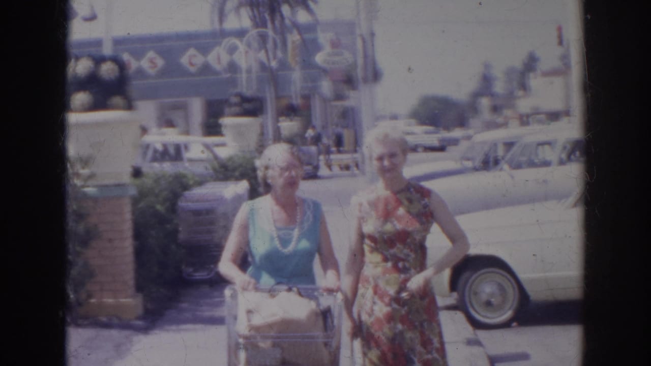 Two elderly women in sleeveless dresses pause or continue forward with groceries in a Norfolk supermarket parking lot in 1966.
