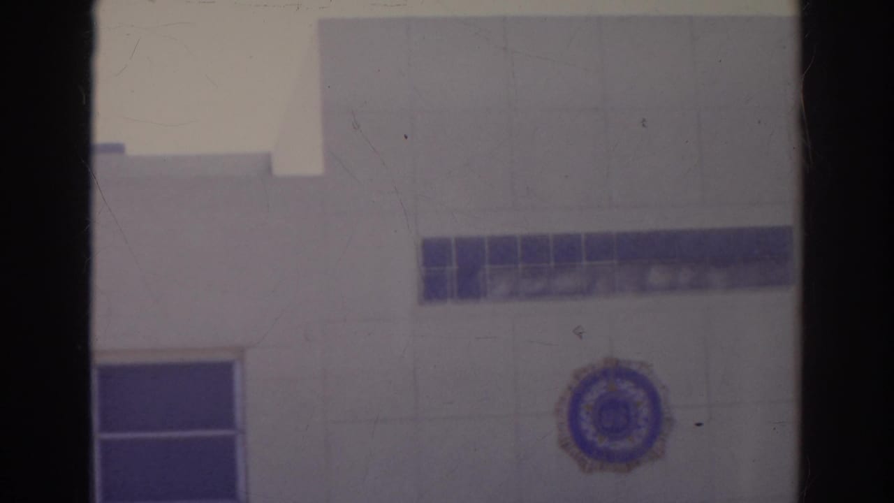 Soft 8mm frame of a white building facade with blue tile bands and a circular emblem.