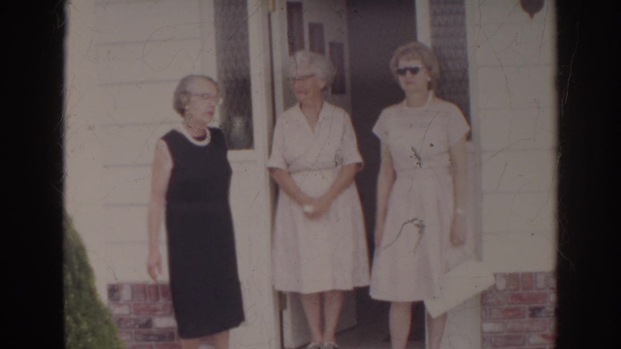 Three adult women in dresses stand near a house doorway.