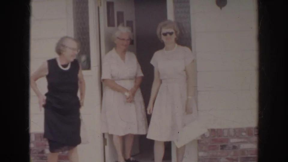 At the Norfolk doorway, one woman in a dark dress steps aside while two women in light dresses stand near the entrance.
