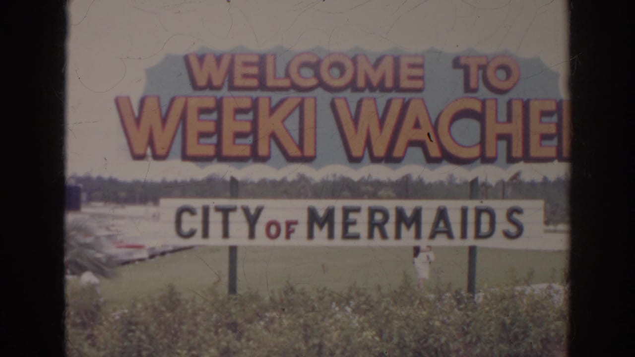 A roadside welcome sign for Weeki Wachee, City of Mermaids, appears in soft 8mm home-movie color.