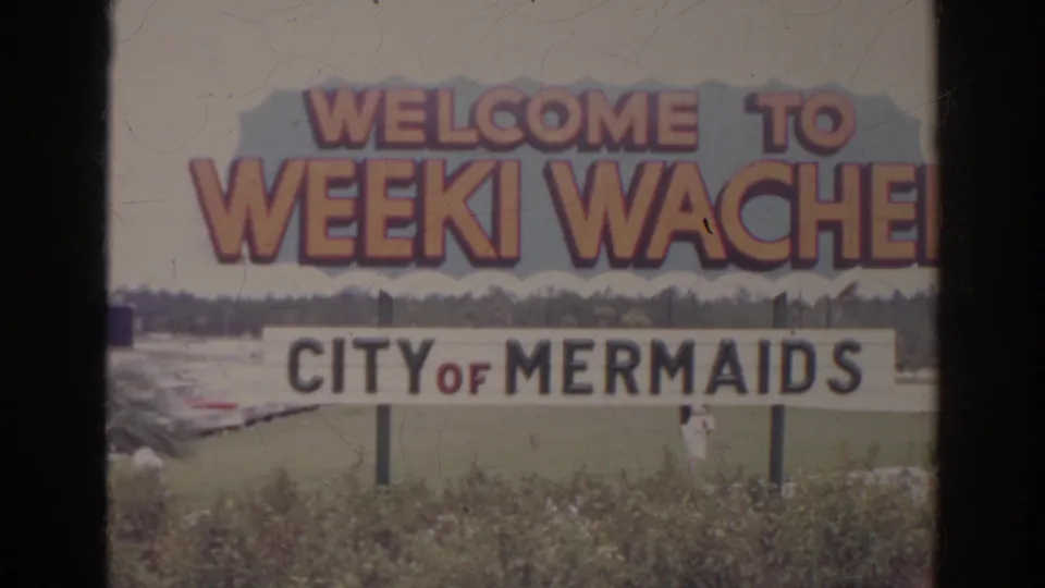 A roadside welcome sign for Weeki Wachee, City of Mermaids, appears in soft 8mm home-movie color.