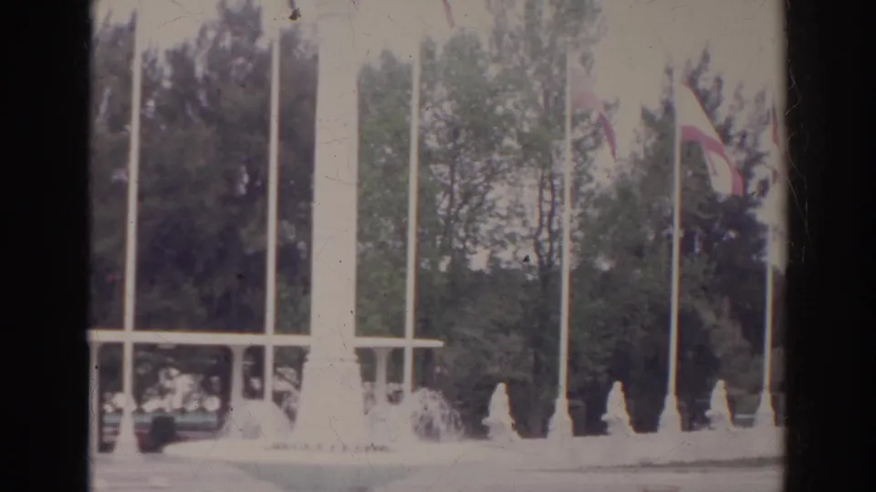 1966 Norfolk, Virginia home-movie frame showing tall flagpoles, international flags, trees, and a white monument or fountain structure.