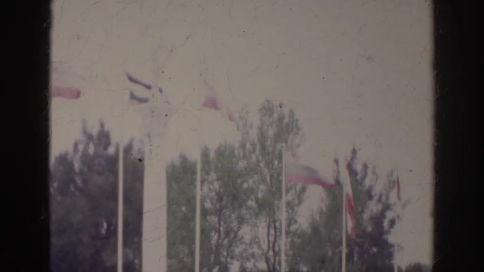 1966 Norfolk, Virginia frame showing multiple flags, tall poles, trees, and the lower edge of a white civic park monument or fountain.