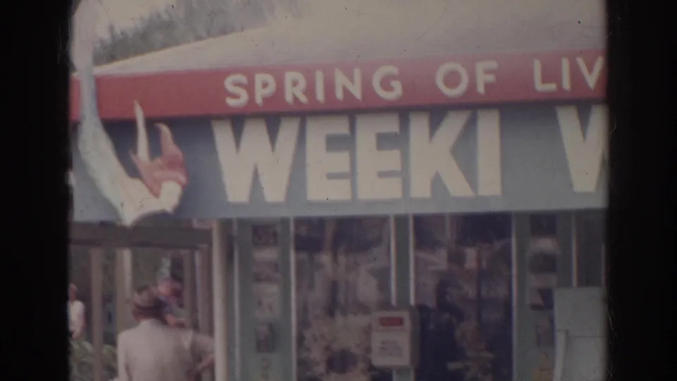 A close 1966 frame shows partial roadside signage with large block letters and small pedestrians near the building.