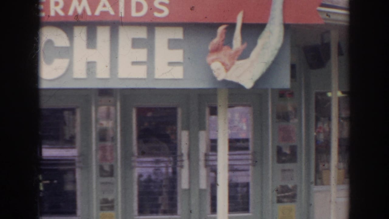 1966 Norfolk home-movie frame showing a partial storefront sign with a mermaid figure above glass entrance doors.