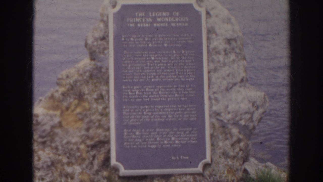Plaque titled The Legend of Princess Wonderful appears mounted on shoreline rocks, with water visible behind it.