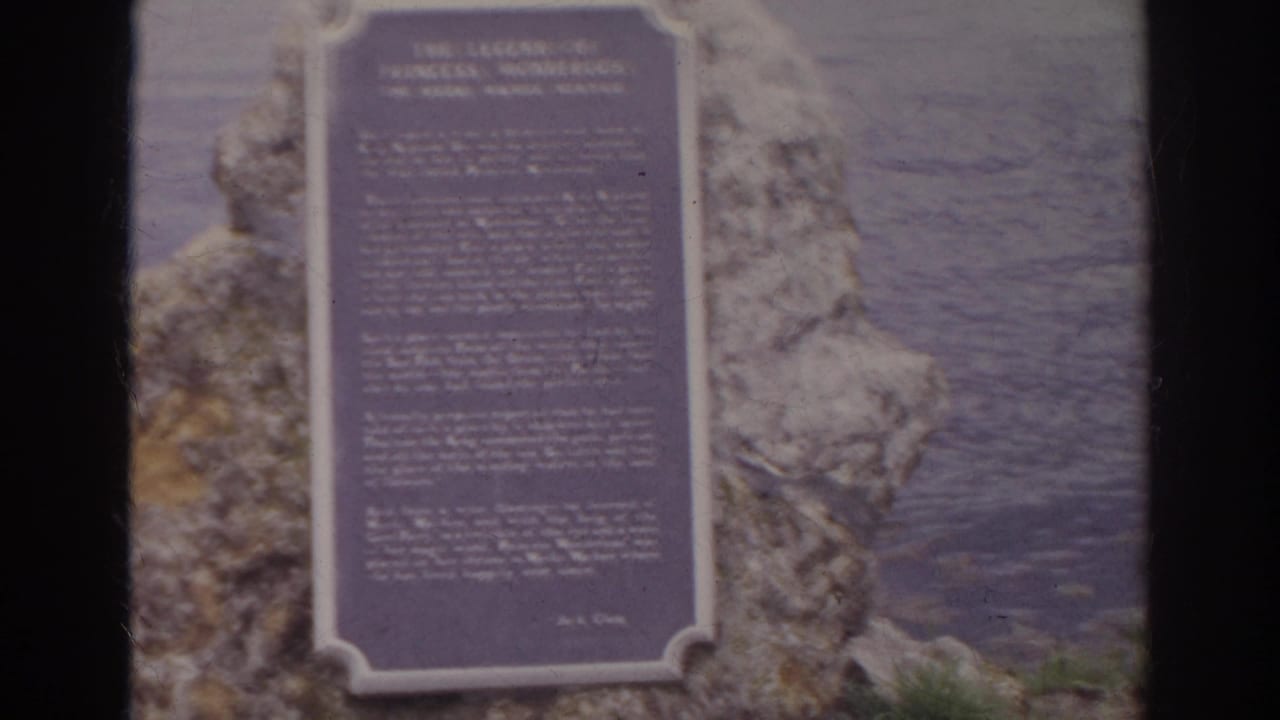Stone plaque mounted on rock beside water, partly obscured by dark film-frame edges.