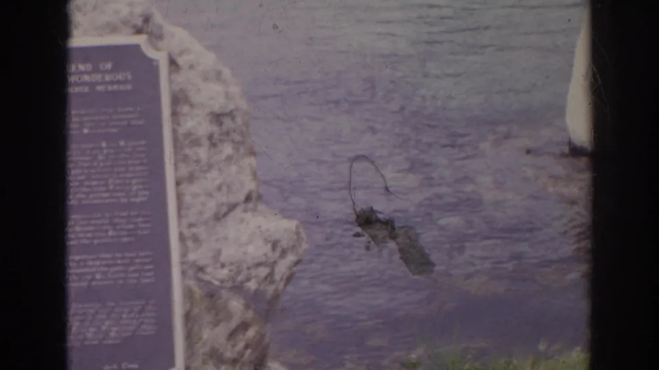 Visitor-shot 1966 Norfolk frame with a plaque set into rock by the water, partly divided by the 8mm frame edge.