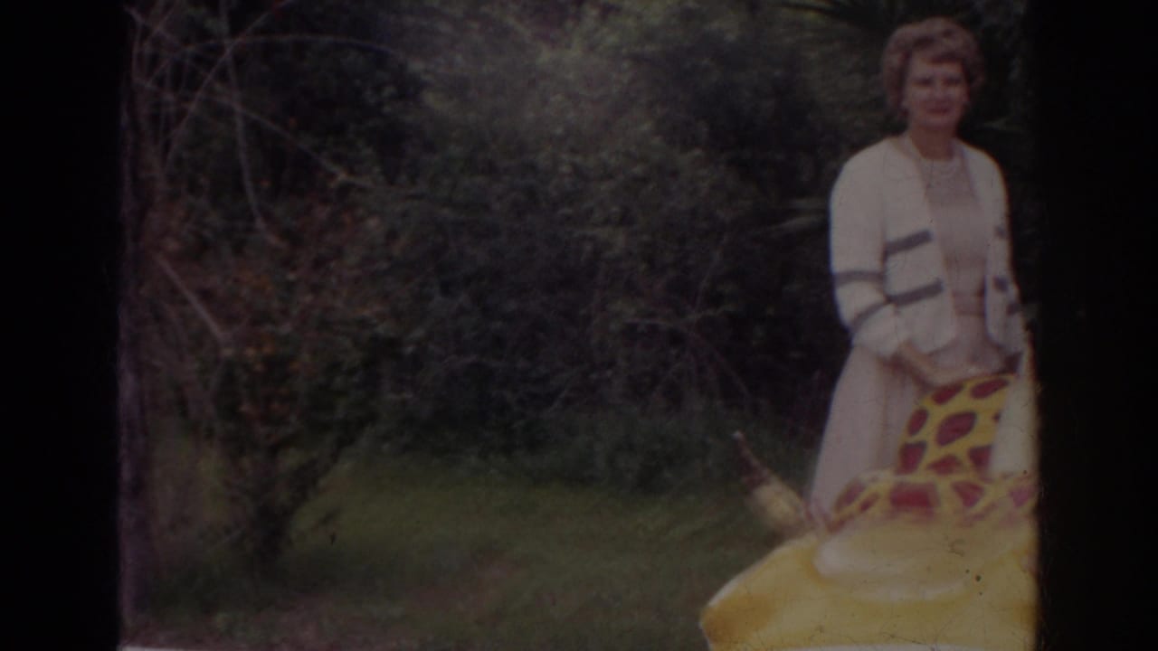 1966 Norfolk home-movie frame with a woman in a cardigan near brush and a large yellow red-spotted inflatable creature.