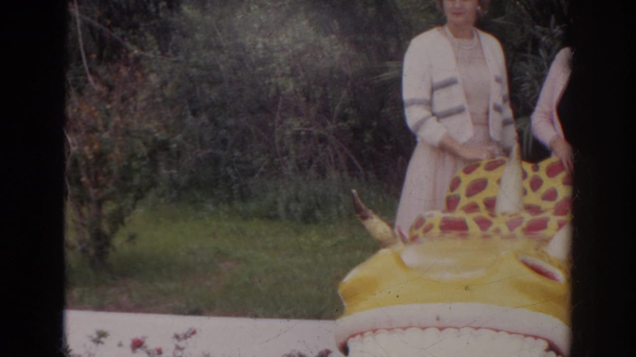 1966 Norfolk 8mm frame showing women partly cropped behind a yellow red-spotted inflatable creature near grass and brush.