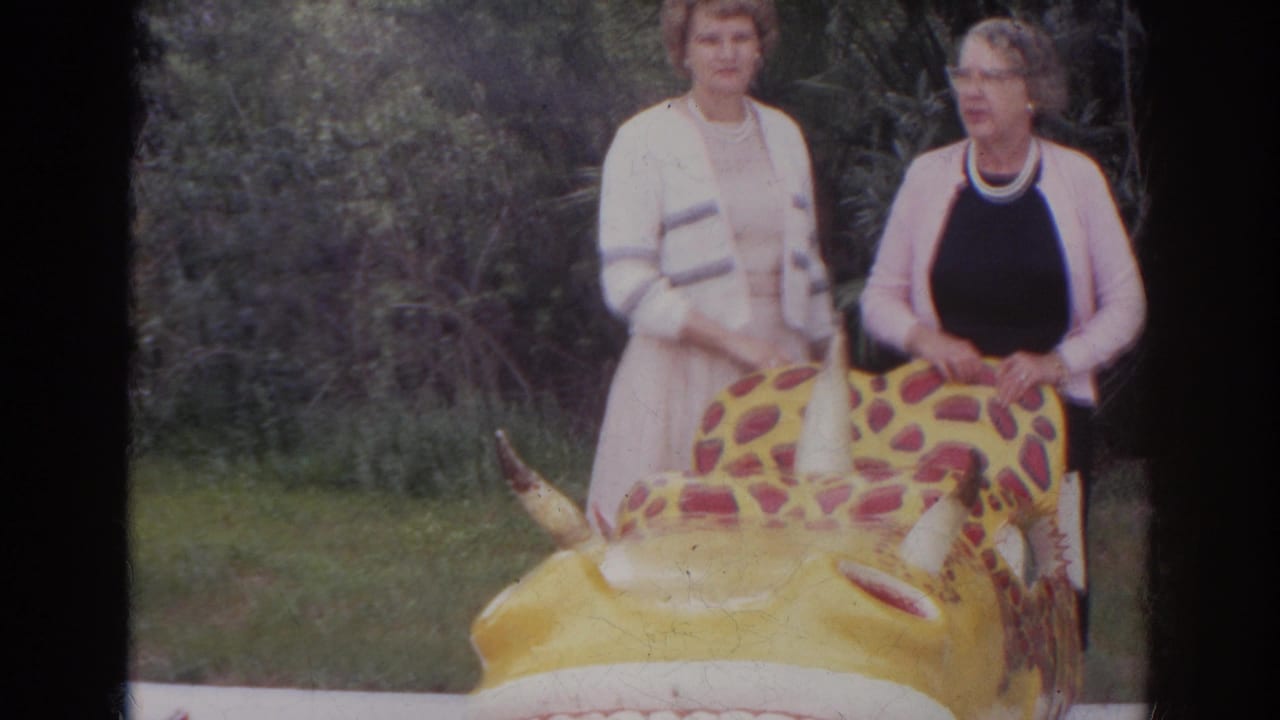 Two women in 1960s dress stand in Norfolk, Virginia near a yellow spotted dinosaur ride in an outdoor attraction setting.
