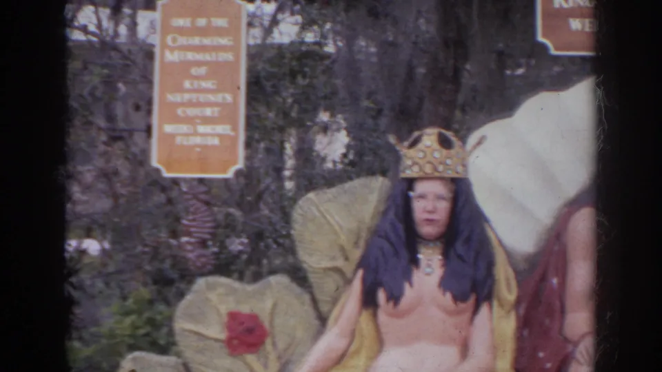 Costumed adult in a crown poses at the King Neptune's Court display with shell-like props and attraction signage visible.