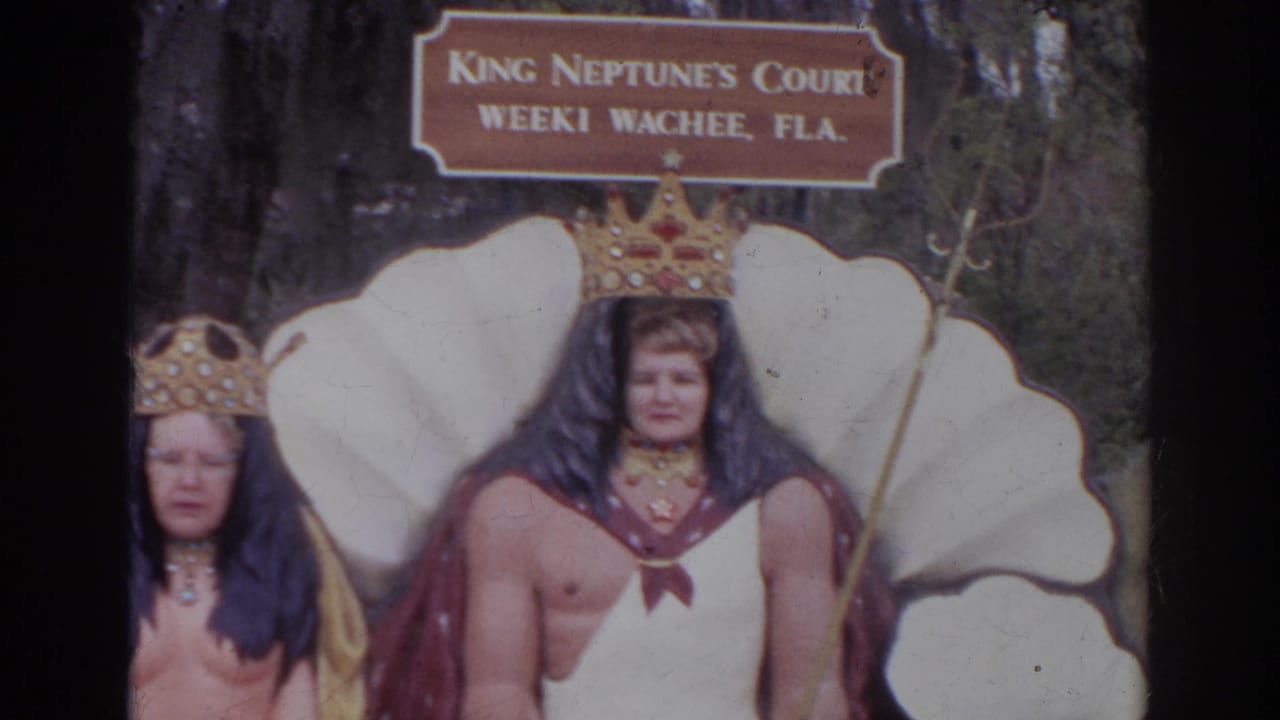 Two costumed figures stand before a shell backdrop and King Neptune's Court sign.