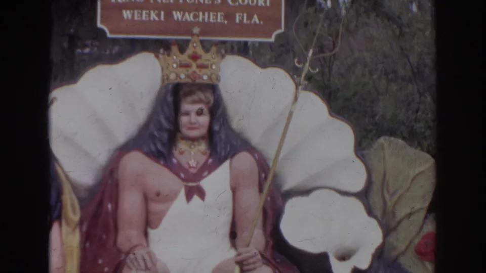 The camera centers on the King Neptune costume figure at the Weeki Wachee display, with the queen partly cropped.