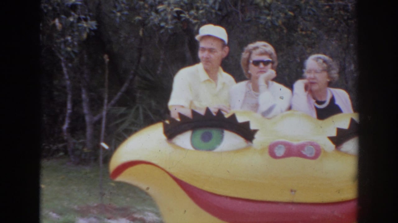 Three adults pose behind the yellow painted attraction display in Norfolk, Virginia, with trees behind them.