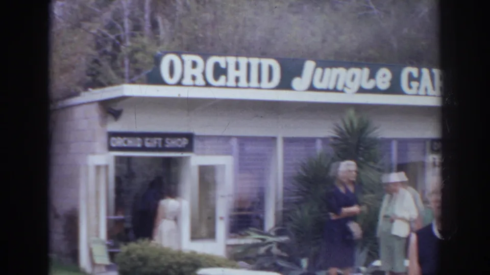 Visitors in 1960s attire stand near the Orchid Gift Shop entrance below the Orchid Jungle Gardens sign in Norfolk.