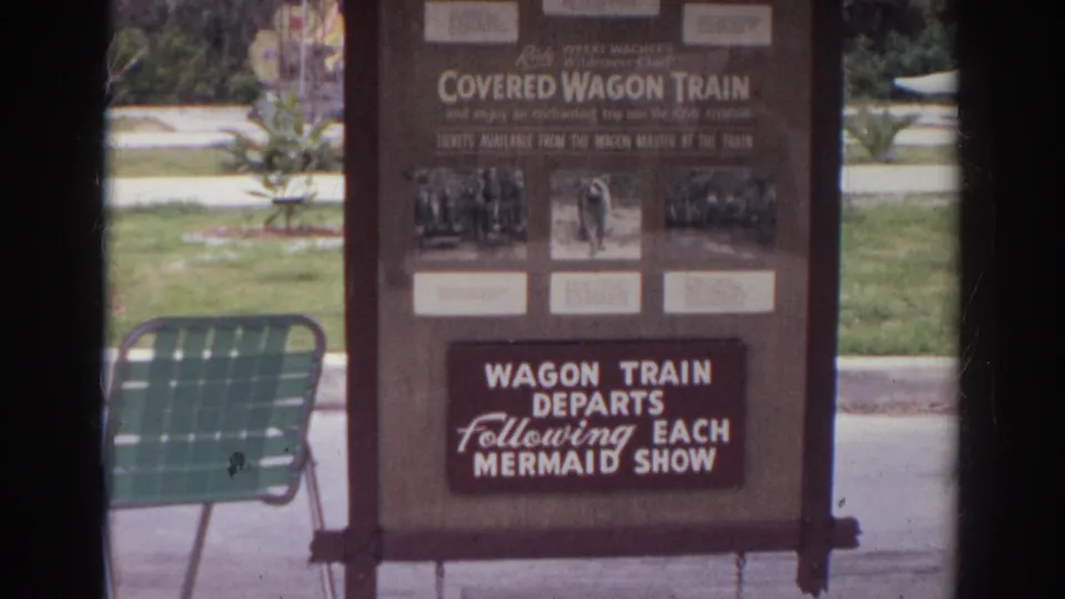 Norfolk, Virginia 1966 home-movie frame showing a Covered Wagon Train attraction sign and nearby green metal chair.