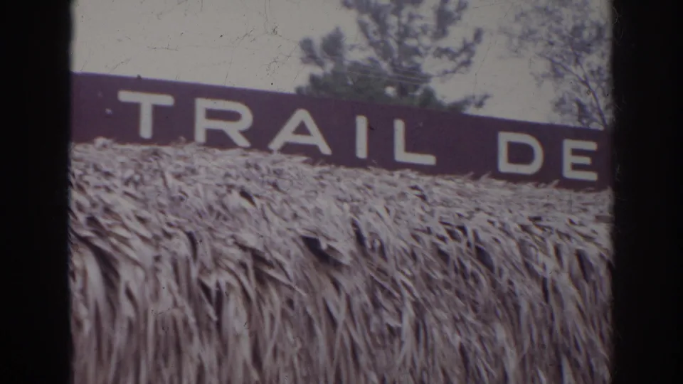 Final Norfolk 1966 frame showing cropped white sign text, including TRAIL DE, above thatched material and background trees.
