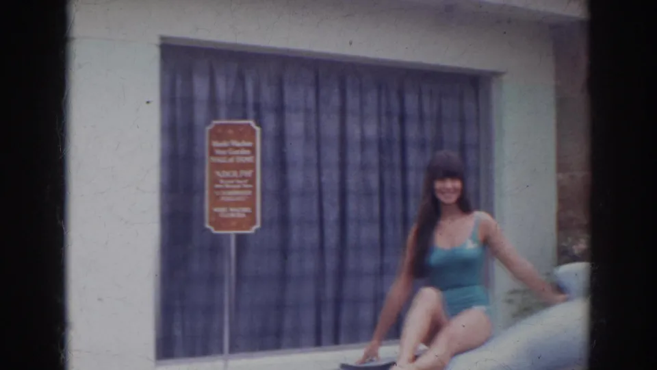 Woman in a teal swimsuit poses on a dolphin statue near a Dolphin Hall of Fame sign in the 1966 Norfolk footage.