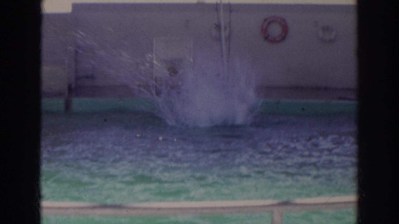 Large splash in an indoor or covered pool viewed through dark film-frame bars.