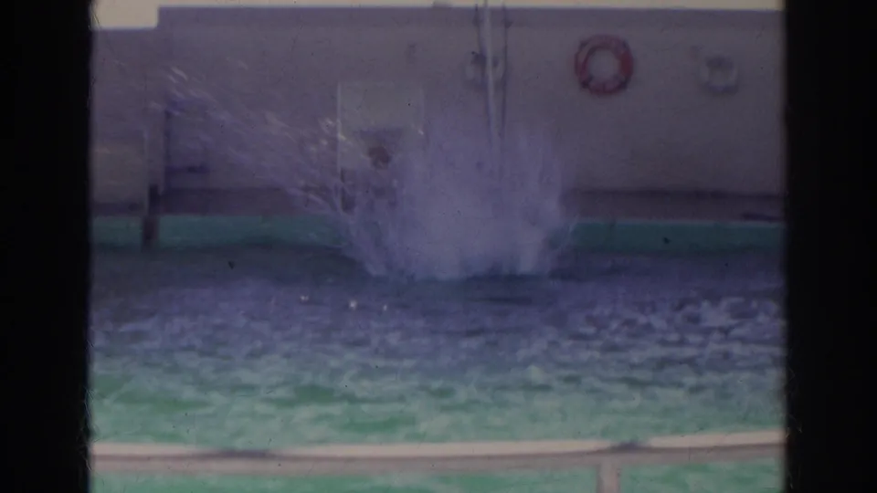 1966 Norfolk natatorium footage shows a swimmer's splash in a green-tinted pool with wall fixtures and railings beyond.