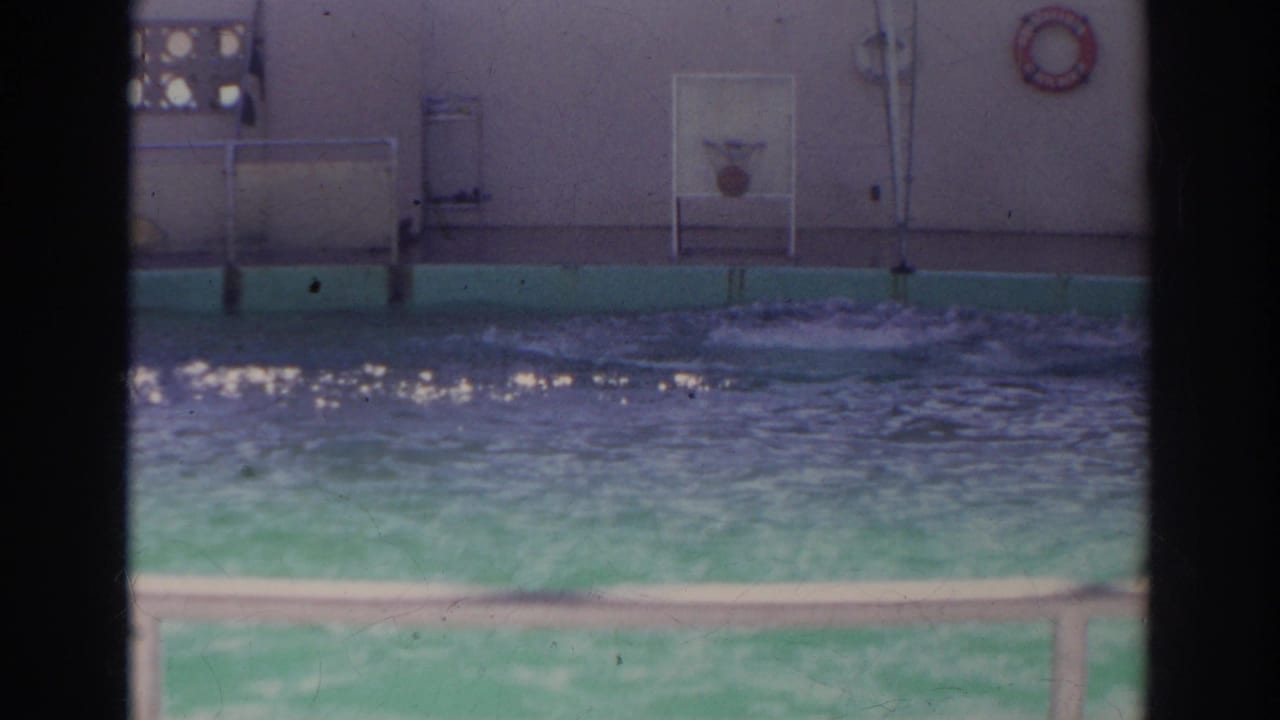 The Norfolk natatorium pool surface ripples after activity, with wall-mounted fixtures and safety equipment visible behind it.