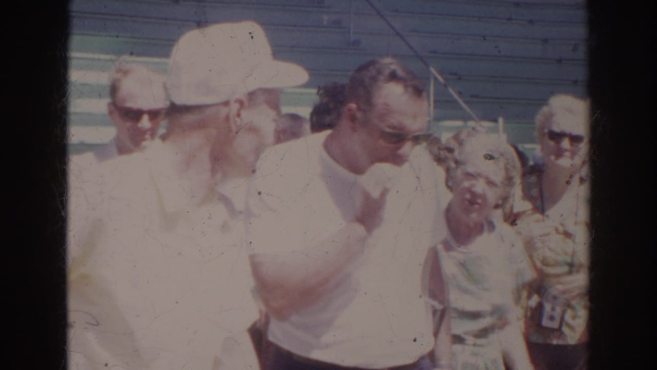 A small spectator group at the Norfolk natatorium appears in bright 1960s sun, with adult faces, bleachers, hats, and sunglasses visible.
