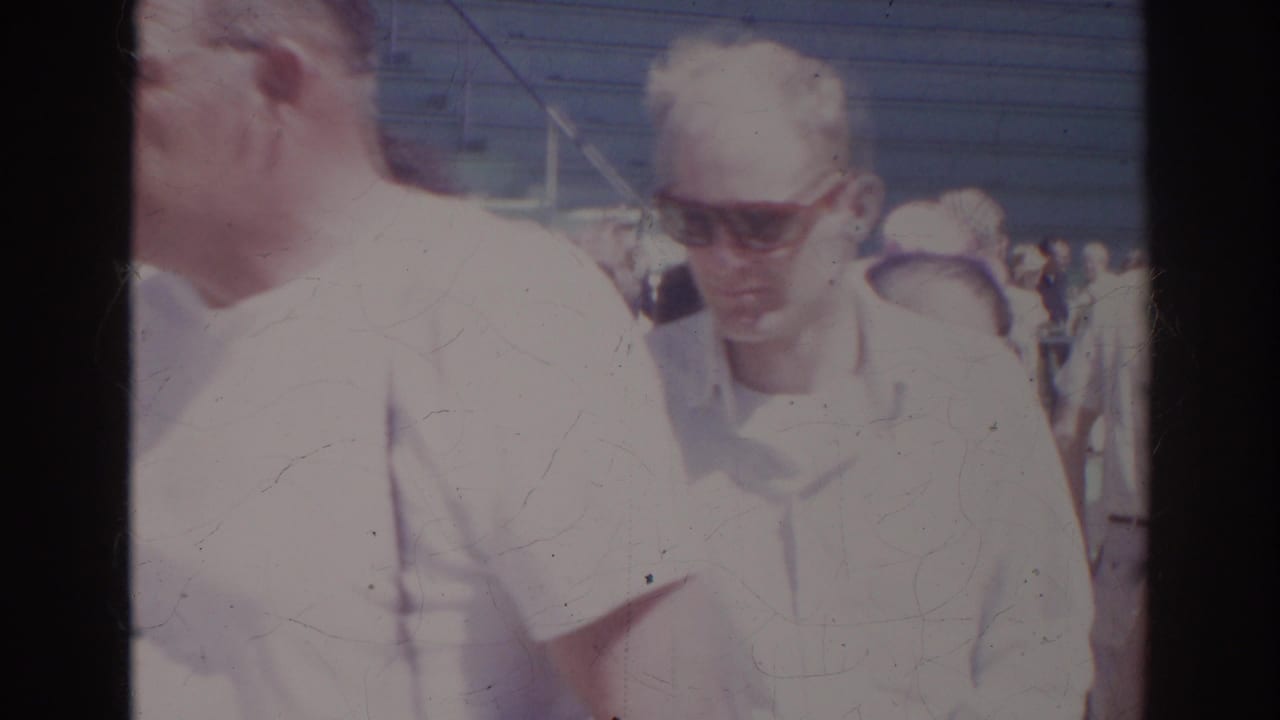 Two adult visitors in light shirts and sunglasses appear in a crowded Norfolk aquarium scene from 1966 home-movie footage.