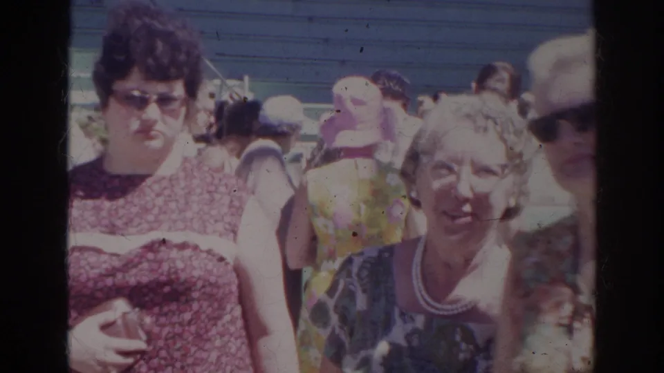 Women in patterned clothing and other visitors gather in a bright Norfolk aquarium crowd in 1966 home-movie footage.
