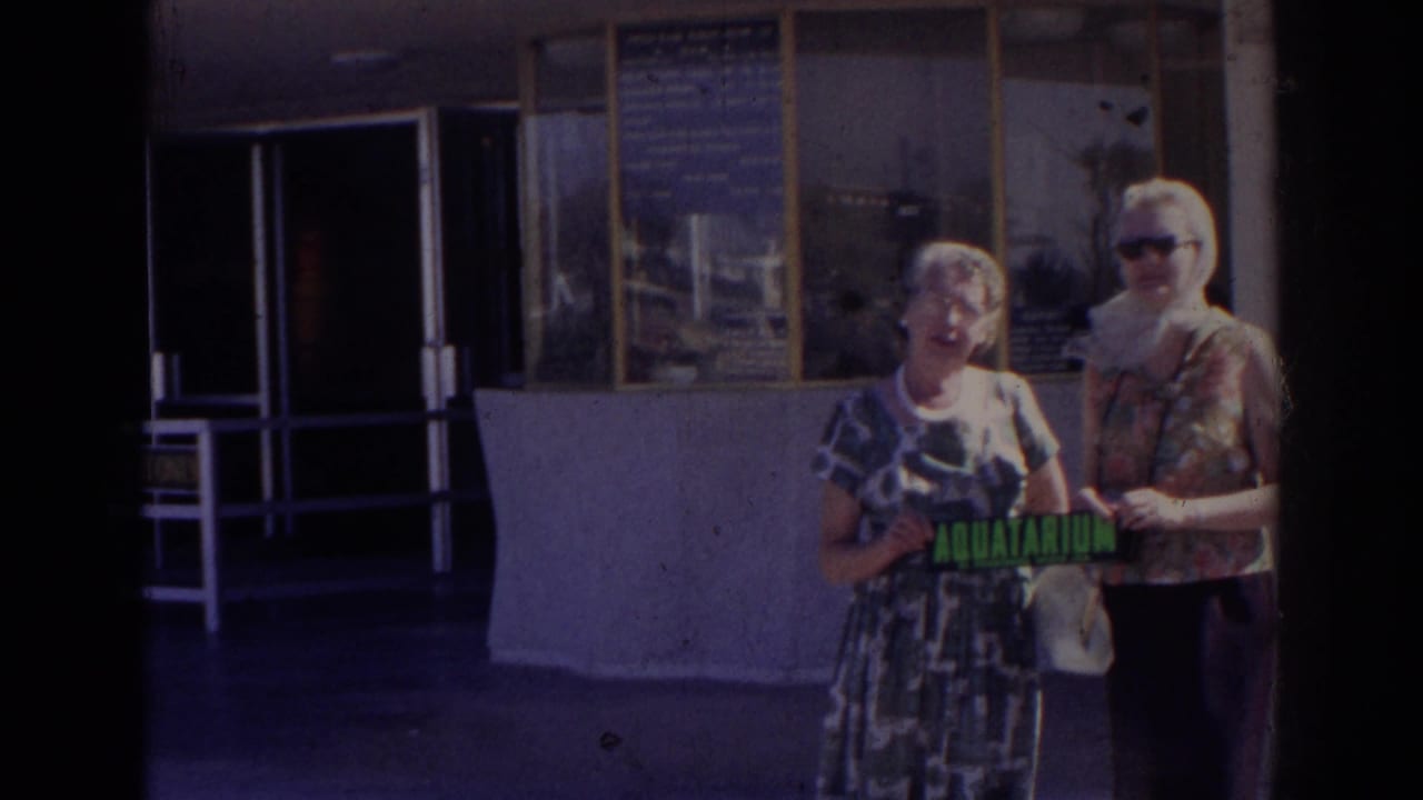 Two women stand near an entrance, one holding an aquarium sign.