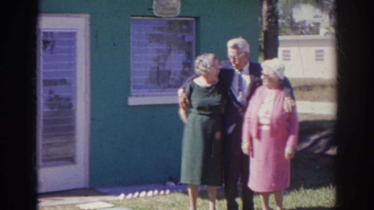 Three older adults pose arm in arm outside a green building in metadata-supported 1966 Norfolk, Virginia home-movie footage.